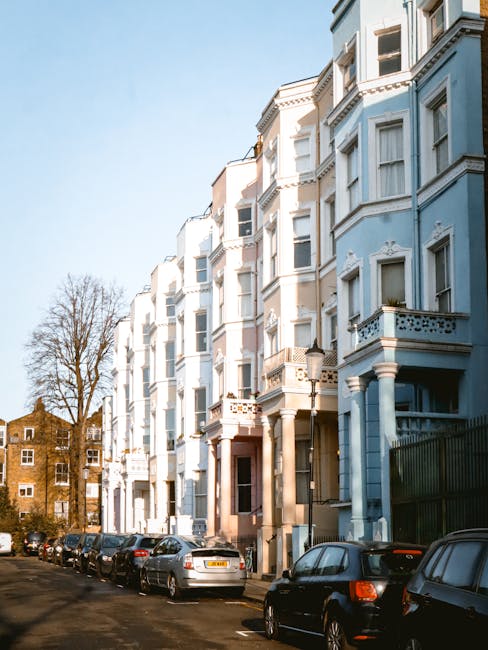 A row of Victorian-style residential buildings painted in pastel blue and white, featuring ornate architectural details such as bay windows, decorative cornices, and small balconies. The buildings are