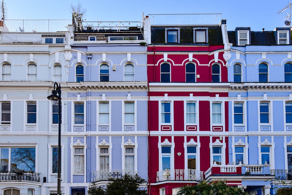 A row of Victorian-style residential buildings painted in pastel blue and white, featuring ornate architectural details such as bay windows, decorative cornices, and small balconies. The buildings are